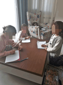 three girls sit at a table with their faces blurred and a puzzle on the floor