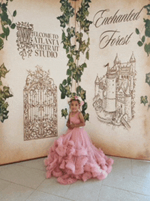 a little girl in a pink dress stands in front of an enchanted forest sign