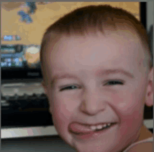 a young boy with his tongue out is smiling in front of a computer screen