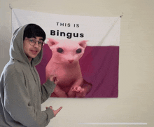 a man in a grey hoodie stands in front of a poster that says this is bingus on it