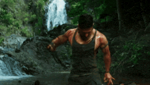 a man in a tank top is standing in front of a waterfall in the woods
