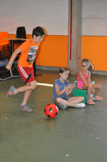 a boy wearing an orange shirt with a picture of a car on it is kicking a ball