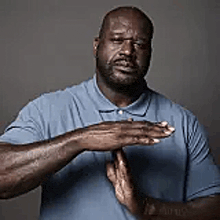 a man in a blue shirt is holding his hands together in front of his face .