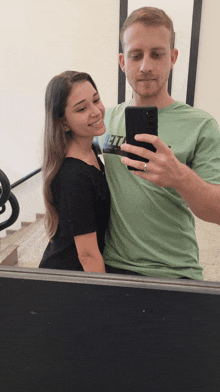 a man in a green shirt takes a selfie with his girlfriend