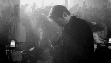 a black and white photo of a man standing in front of a crowd of people in a club .