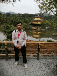 a man with a lanyard around his neck stands in front of a pond with a building in the background