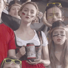 a group of people are sitting in a stadium watching a game and one woman is holding a mug .