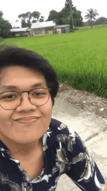 a man wearing glasses is smiling in front of a field of green grass