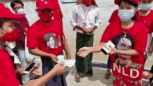 a group of people wearing face masks and red shirts are standing next to each other on a dock .