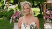 a woman in a wedding dress holds a bouquet of flowers in front of a sign that says heart and home