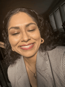 a woman with curly hair is smiling and wearing a plaid jacket