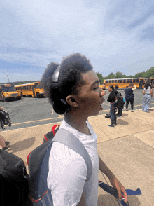 a boy wearing headphones stands in front of a row of yellow school buses