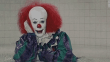 a scary clown is sitting on the floor in a bathroom .