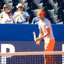 a man is holding a tennis racquet on a tennis court in front of a blue wall with the letter d on it