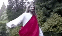 jesus is wearing a red robe and a white robe and is dancing in the woods .