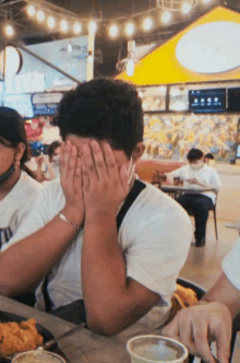 a man covering his face with his hands while sitting at a table in a restaurant