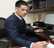 a man in a suit and tie sits at a desk with a dell computer