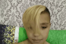 a young boy with blonde hair and a shaved head is laying on a bed .