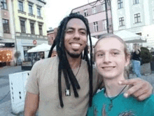 a man with dreadlocks is posing for a picture with a young boy in front of a building .