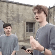 two young men are standing next to each other in front of a wall . one of the men is holding a flashlight .