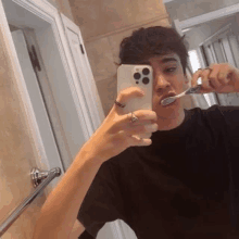 a man is brushing his teeth in front of a mirror while taking a selfie with his phone .