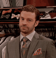 a man in a suit and tie is standing in front of a closet filled with shirts and ties .