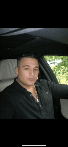 a man wearing a black shirt and a gold chain is sitting in a car