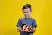 a young boy is holding a picture of a man 's face in his hands