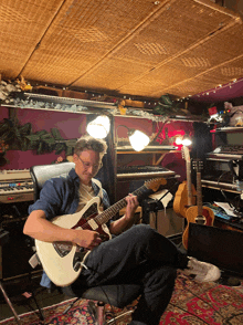 a man sits in a chair playing a guitar in a room