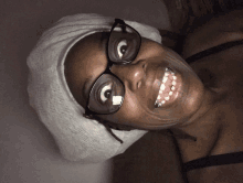 a woman wearing glasses and a towel on her head smiles for the camera