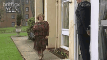 a woman in a red dress walks down a sidewalk in front of a building with britbox written on the top