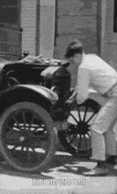 a black and white photo of a man working on an old car on the side of the road .