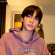 a young man wearing a purple hoodie and a chain necklace says fighting