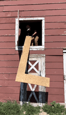 a man holds a piece of wood in front of a red barn