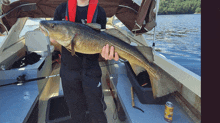 a man holding a large fish on a boat with a can of beer next to him