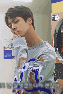 a young man is standing in front of a washing machine in a laundromat and covering his mouth with his hand .