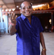 a man wearing glasses and a blue shirt is laughing and waving .