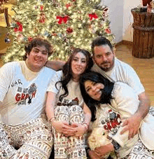 a group of people are sitting in front of a christmas tree holding a teddy bear .