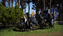 a group of men in armor are walking in a field with a blue banner that says ' knight ' on it