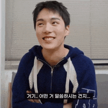 a young man wearing a blue sweater with a white stripe on the sleeves is smiling