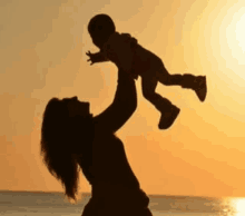 a silhouette of a woman holding a baby in the air at sunset .