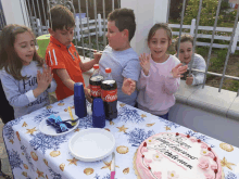 a group of children celebrate a birthday with a cake and coca-cola