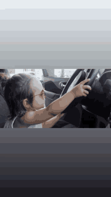 a little girl wearing glasses is sitting in a car and pointing at the steering wheel