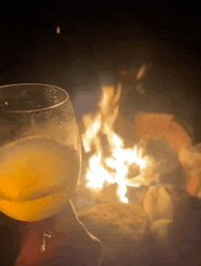 a glass of beer is sitting in front of a campfire .