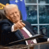 a man in a suit and tie is sitting at a table and pointing at the camera .