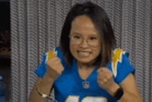 a woman wearing a blue jersey and glasses is making a fist gesture .