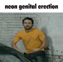 a man in a yellow shirt is standing in front of a brick wall with the words neon genital erection below him .