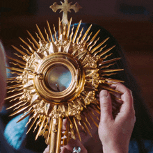 a person is holding a gold object with a cross on it