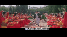 a man in a black jacket is surrounded by women in red dresses holding trays of food and flowers