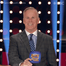 a man in a suit and tie is holding a family feud canada card